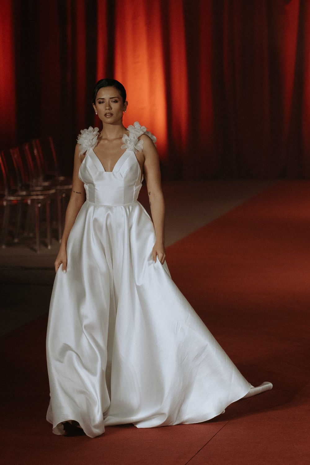 Model walks runway in flowing white voluminous gown with dramatic silhouette during fashion show presentation.