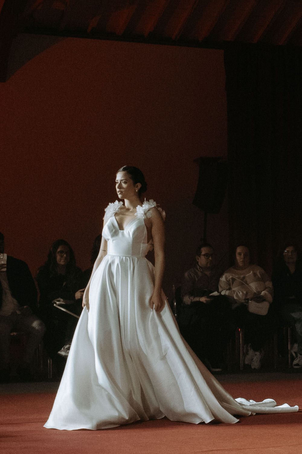 A dancer in a flowing white dress performs an expressive contemporary dance piece on a dark stage.