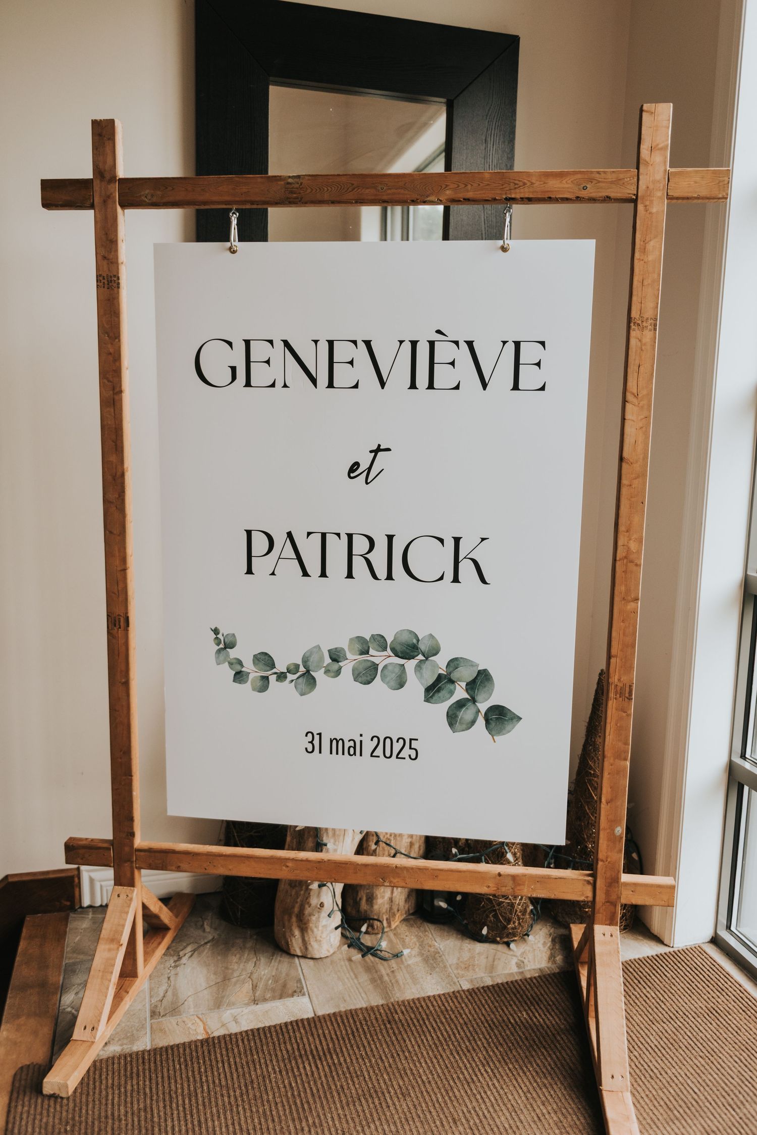 Wedding signage displays 'Genevieve et Patrick' on wooden easels with eucalyptus leaf decorations and minimalist design.