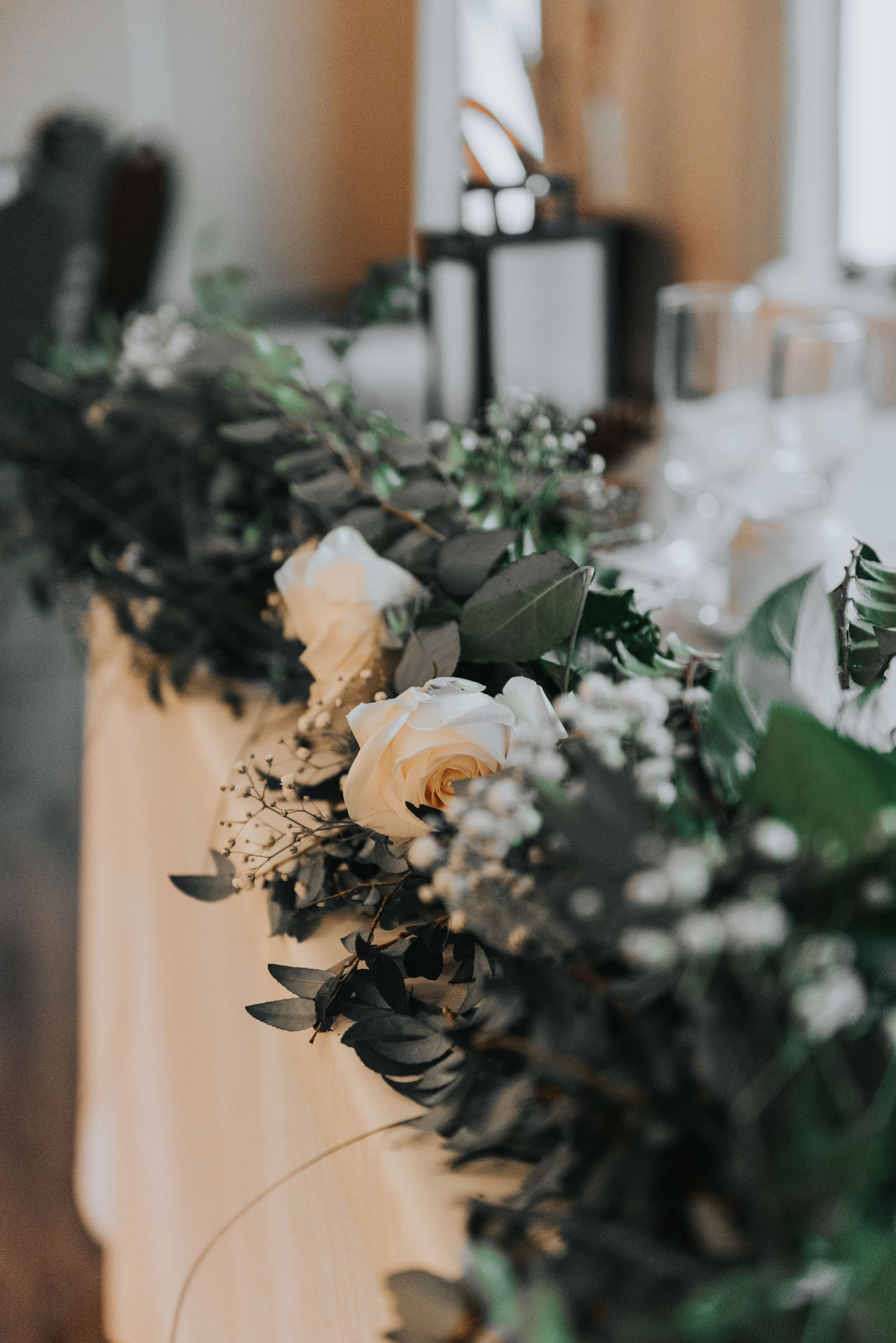 Elegant floral wedding decor features white roses and eucalyptus greenery arranged along a reception table setting.