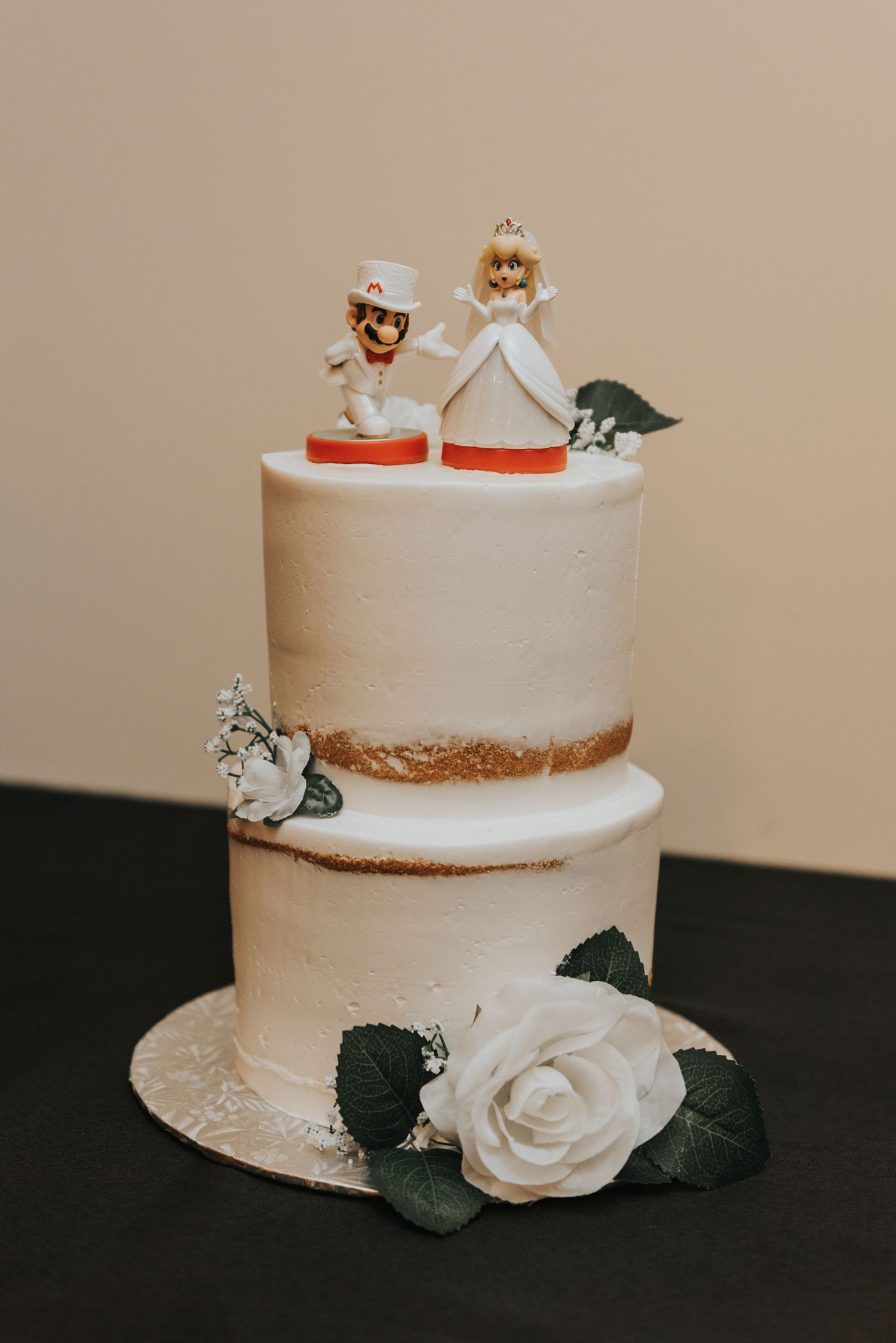 A white wedding cake with delicate rose decorations and small figurine toppers shown from multiple angles.