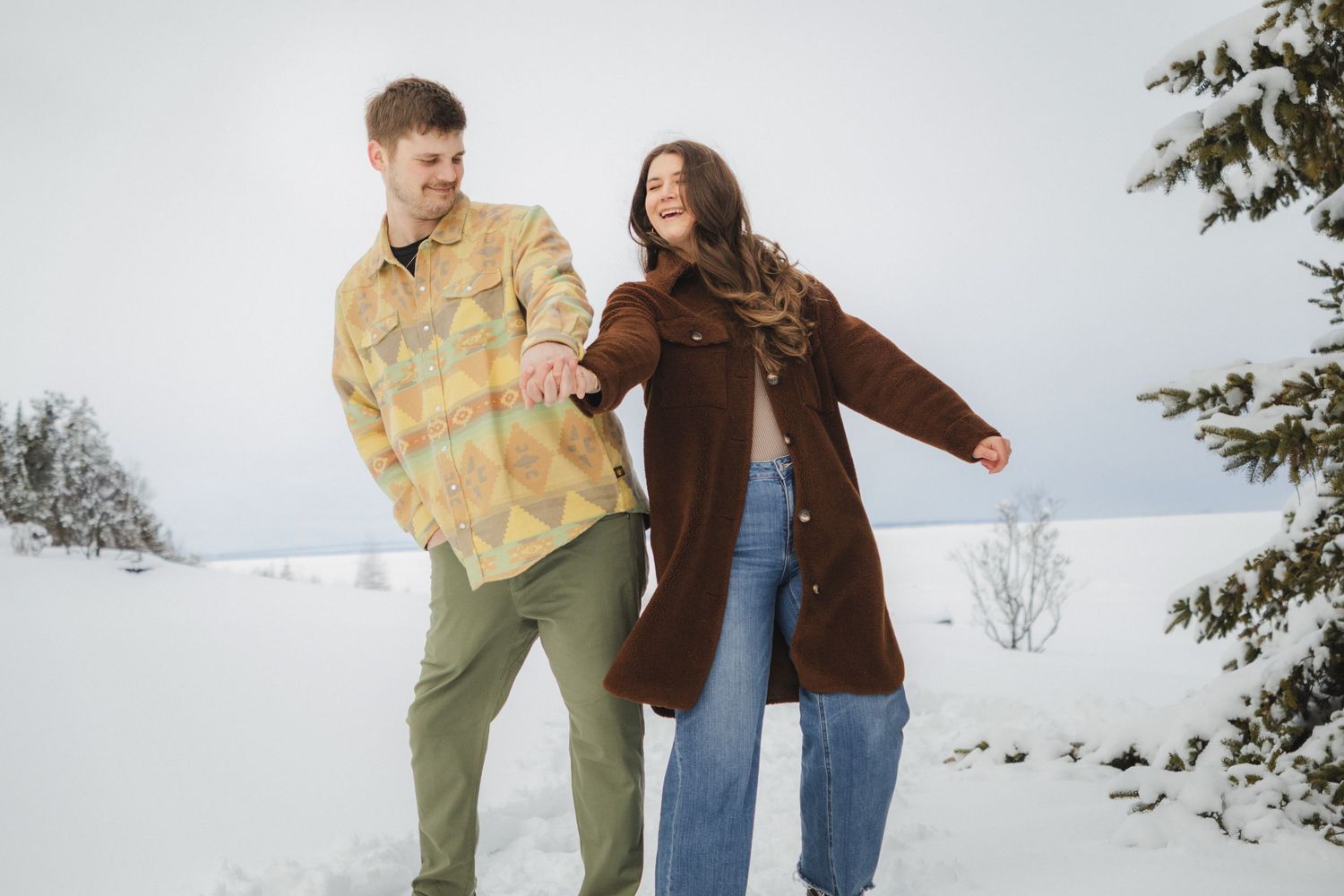 Two people in winter clothing laughing and playing together in a snowy outdoor setting.