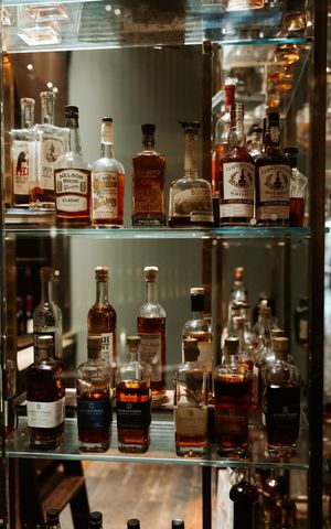 Display of various whiskey and bourbon bottles on glass shelves with ambient lighting.