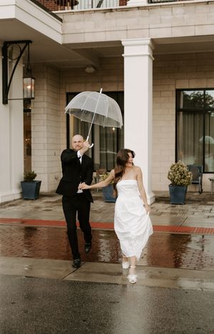 Playful sequence of a couple dancing with umbrellas on a wet sidewalk outside a building.