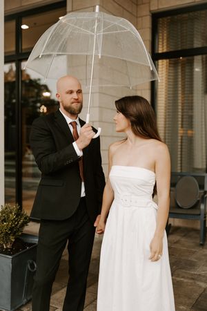 A couple shares sweet moments under a clear umbrella on a covered walkway.
