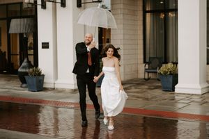 A couple playfully moves along a covered walkway during a rainy day photoshoot.