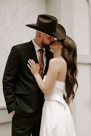 Romantic couple embraces in front of modern white building with clean lines.