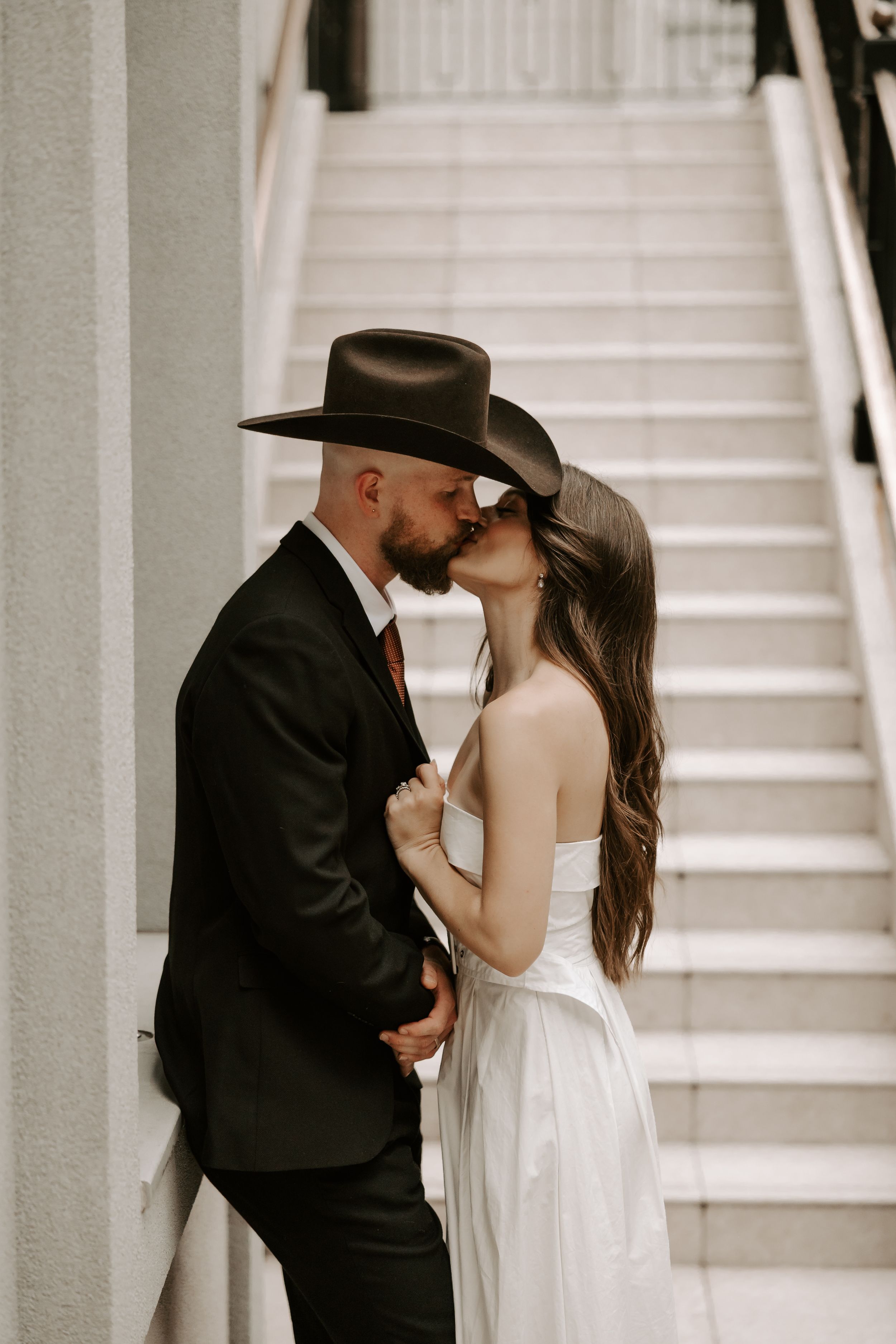 Couple in wedding attire sharing a romantic moment by white staircase.