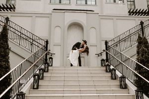 A couple embraces on an elegant white staircase with symmetrical railings and architectural details.