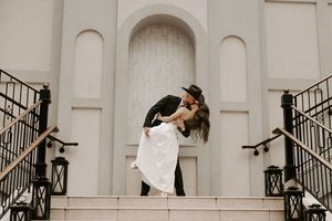 A romantic wedding couple shares a passionate kiss on grand white stone steps with decorative railings.