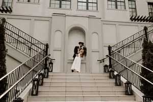A romantic moment captured on an elegant white staircase with black iron railings and lanterns.