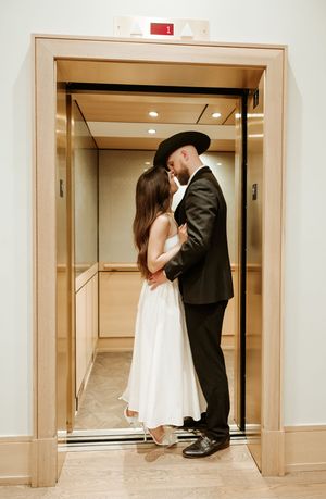 Wedding couple embraces in front of modern elevator doors.