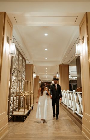 A couple walks down an elegant hotel hallway with cream colored walls and modern lighting fixtures.