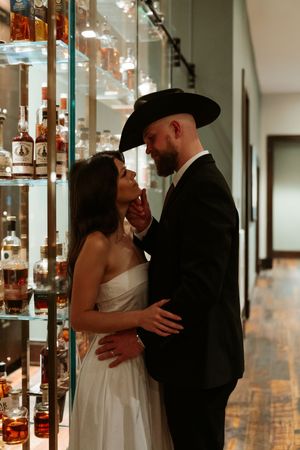 Intimate moment captured between a couple standing near glass shelves filled with bottles.