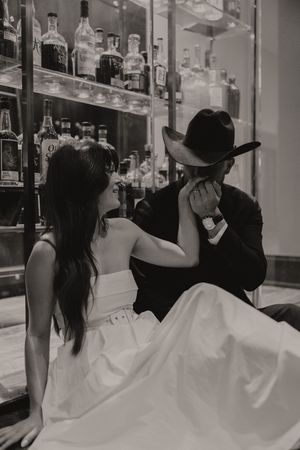 Monochrome image of a couple in formal wear near illuminated bottle displays.
