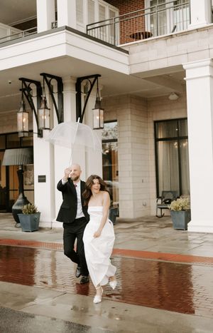 A couple dances in the rain outside a modern building with white columns.