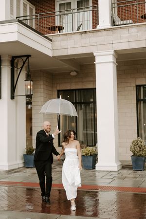 A couple shares a playful moment under white columns during a rainy wedding photoshoot.