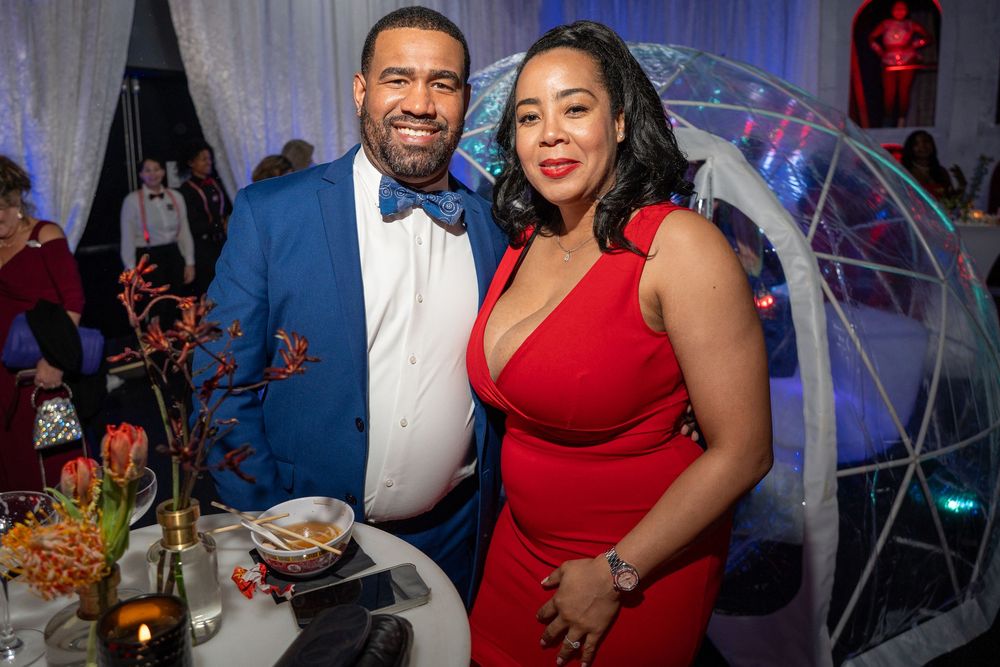 Guests in formal attire enjoying an elegant evening event with red and blue lighting accents.