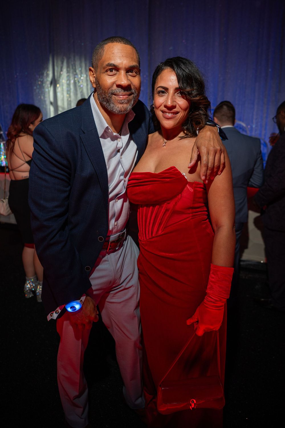 A couple poses at an elegant event, with the woman wearing a stunning red dress and long gloves.