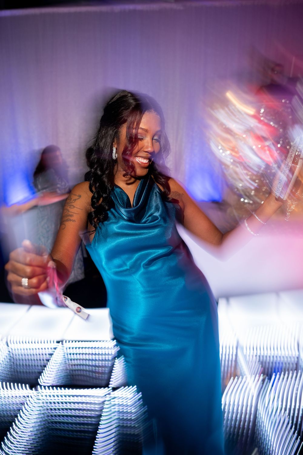 A person in a turquoise top dances energetically against a backdrop of glowing lights creating a motion blur effect.