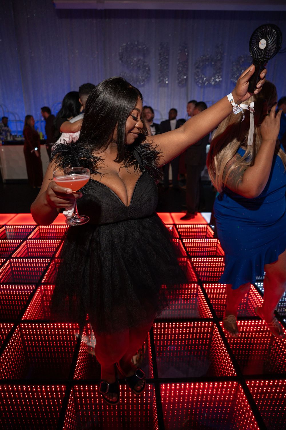 People dancing and enjoying drinks at a nightclub with red LED lighting along the bar counter.