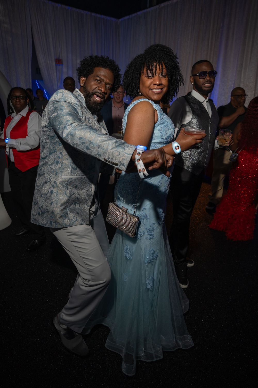 Dancers in formal attire move energetically across a dark dance floor at what appears to be a wedding reception.