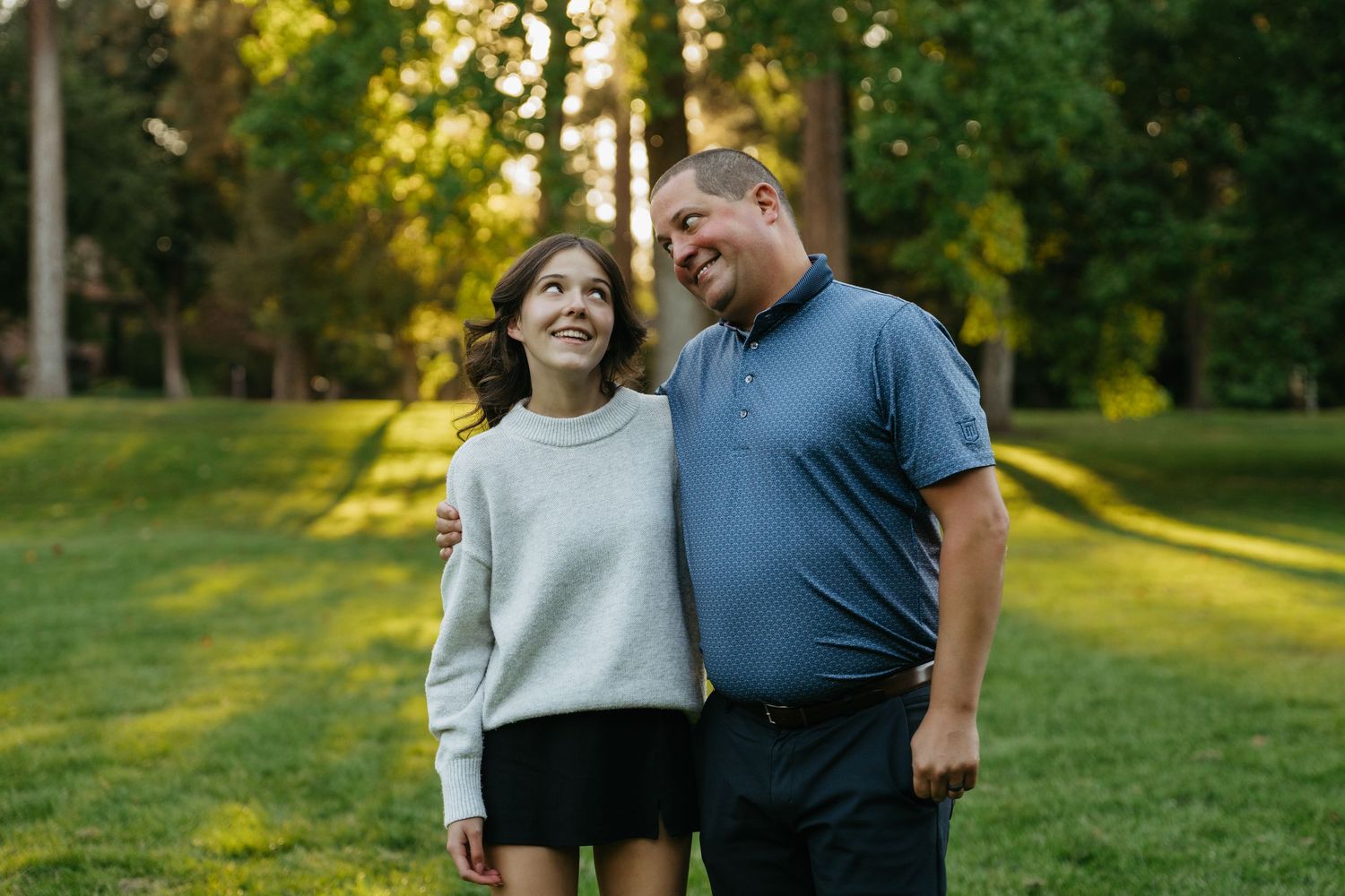 A couple laughs together while walking through a sunlit park during golden hour.
