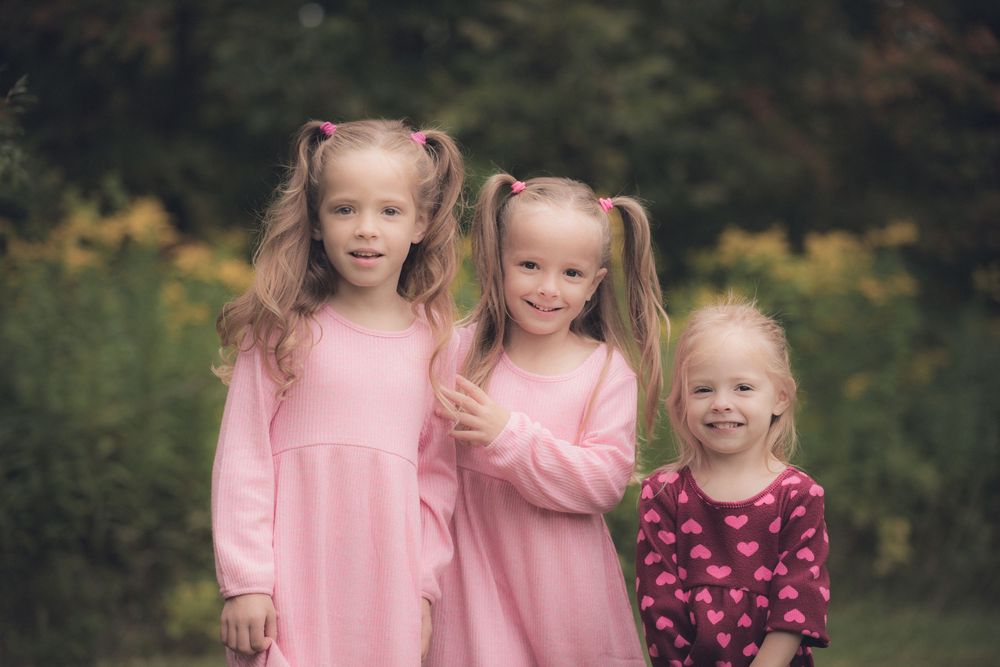 Three young girls in pink dresses pose together for a portrait in a garden setting.