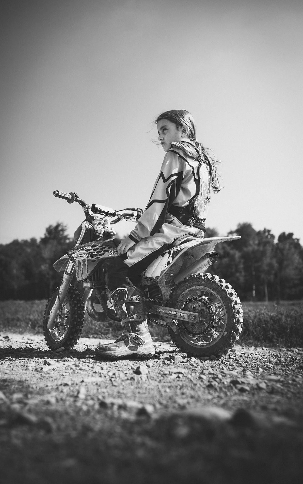 A dirt bike rider sits on their motorcycle in a dramatic black and white photograph.