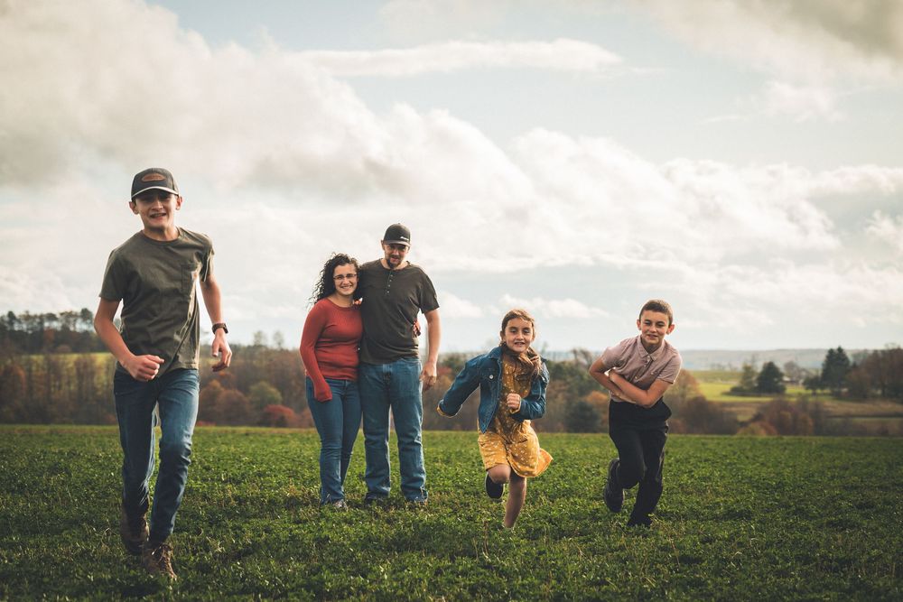 Family runs together through a grassy field on a cloudy autumn day.