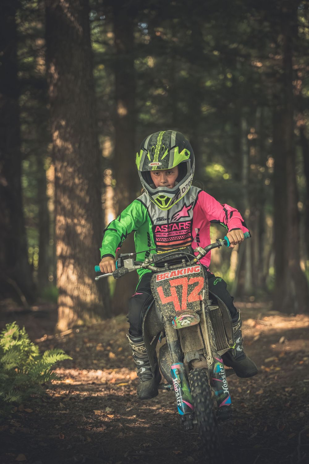Motocross rider in bright green gear rides through a forest trail.