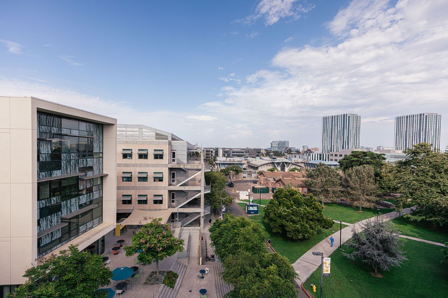 Panoramic view of modern university campus buildings with glass facades under blue sky and white clouds.