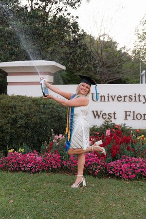 Cheerleader performs high kicks in front of a university sign with blooming pink flowers in the background.