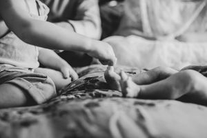 Black and white photo of toddler and newborn baby feet on a soft bed.