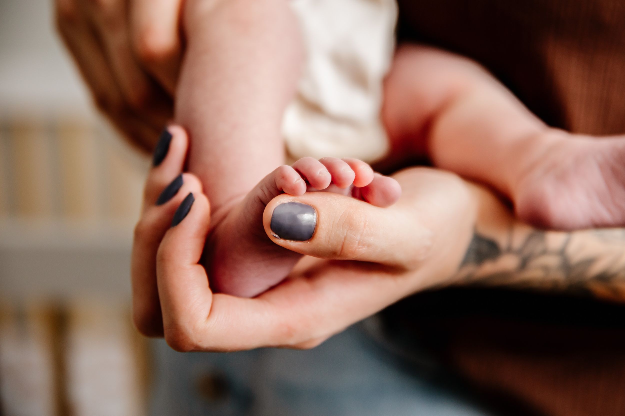 Close-up of adult hands with tattoo gently holding tiny newborn baby feet.