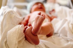 Newborn baby lying on white hospital blankets with tiny feet raised in the air.
