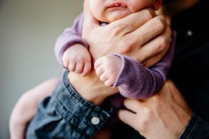 Close up of newborn baby feet and tiny hands held by parent in denim shirt.
