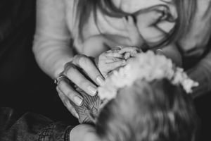 Black and white photo of grandparent holding newborn babys tiny hand with flower headband.