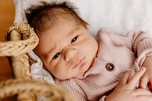 Newborn baby in pink onesie lying in a wicker basket with a gentle expression.