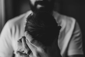 Bearded man tenderly cradling a newborn baby's head in black and white photo.