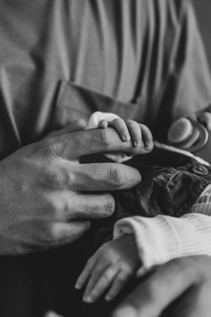 Black and white photo of an adult hand gently holding a newborn baby's tiny hand, symbolizing love and parenthood.