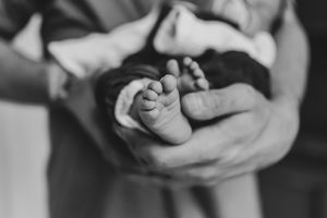 Black and white photo of a newborn baby's tiny feet cradled gently in an adult's hands.