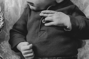 Black and white close-up of a baby in a waffle-knit henley shirt touching a button.