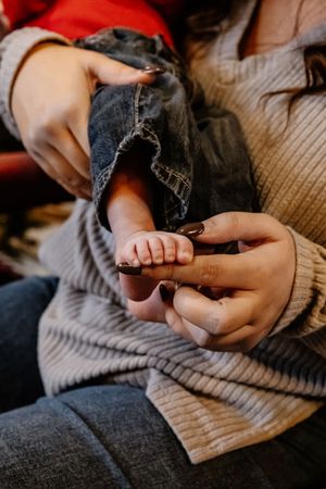 Mother holding her newborn baby's tiny feet in her hands while sitting down.