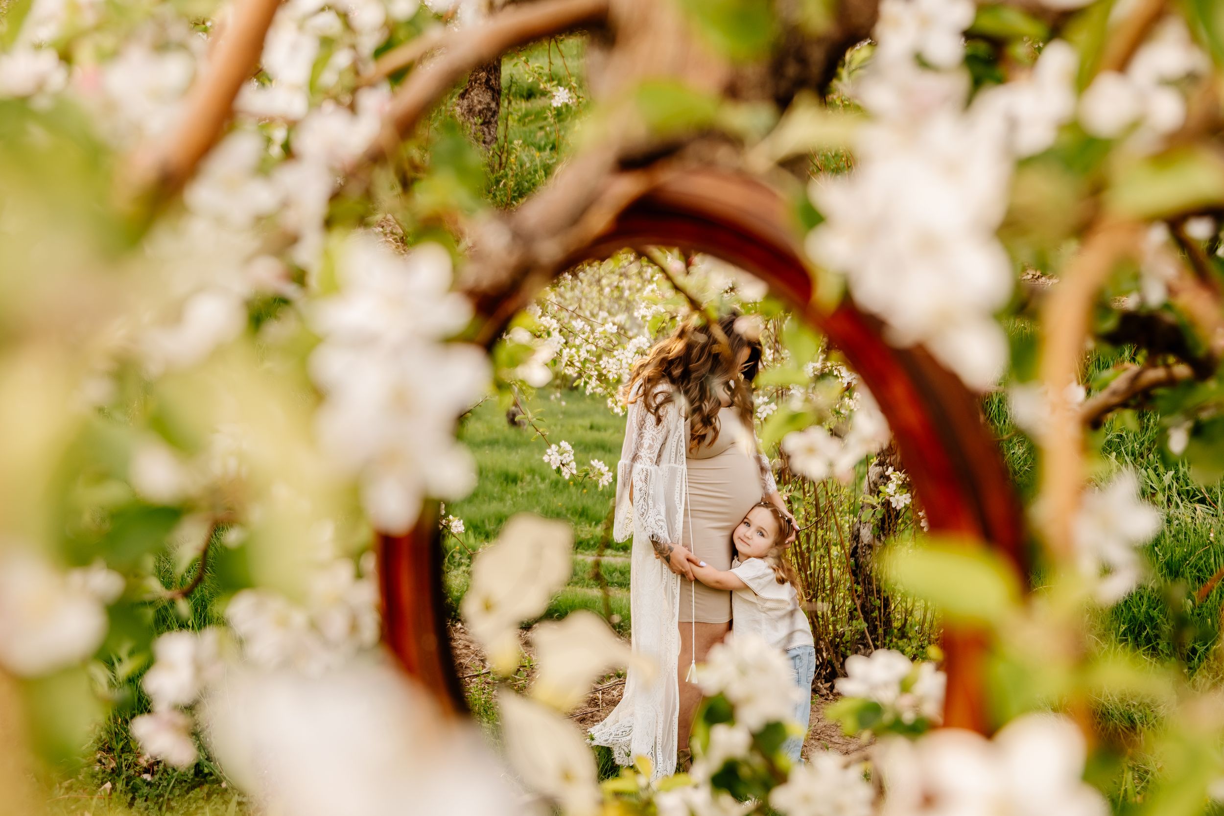 Mother and child embracing in a blooming spring garden framed by white apple blossoms and lush greenery.