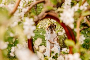 Mother and child embracing in a blooming spring garden framed by white apple blossoms and lush greenery.