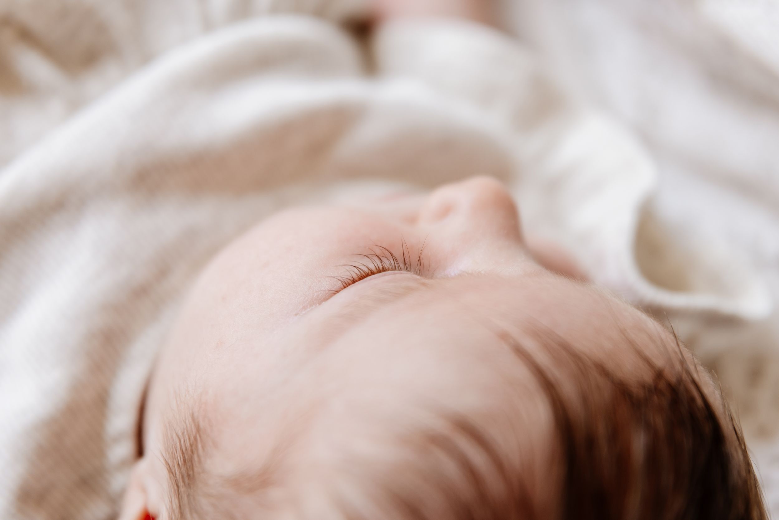 Close-up of a sleeping newborn baby with delicate eyelashes, wrapped in a soft white blanket.