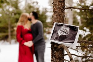 Ultrasound photo propped on tree with couple kissing behind it in snowy winter forest.