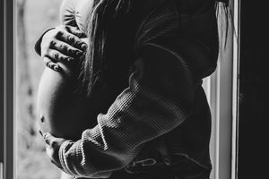 Black and white photo of a couple embracing near a window during pregnancy.