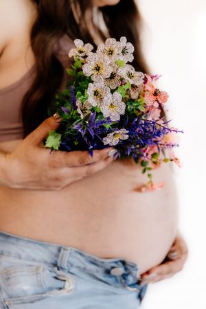 Pregnant woman holding a colorful wildflower bouquet against her bare baby bump.